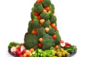 Holiday themed veggie tray with a star topped broccoli Christmas tree and an assortment of carrots, radishes, celery, tomatoes, peppers, and olives.