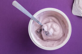 Yogurt cup with blue berry yoghurt, spoon and foil lid isolated on purple background - top view photograph