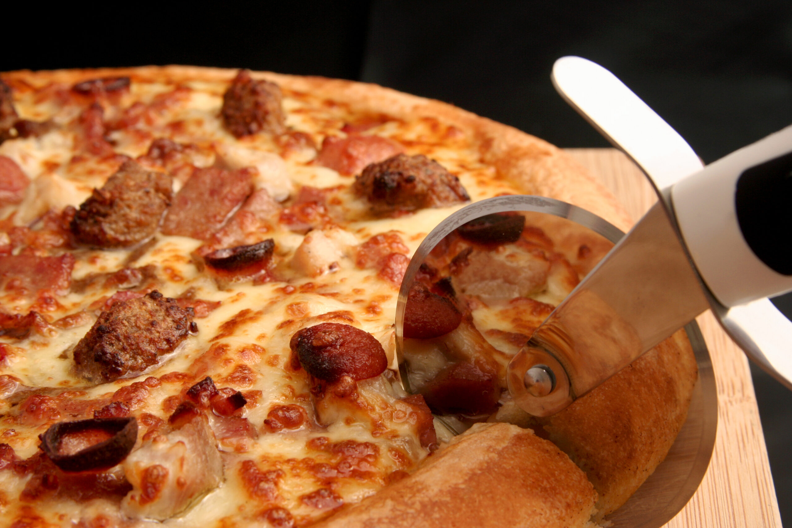 Pizza cutter slicing through a meat lovers deep pan