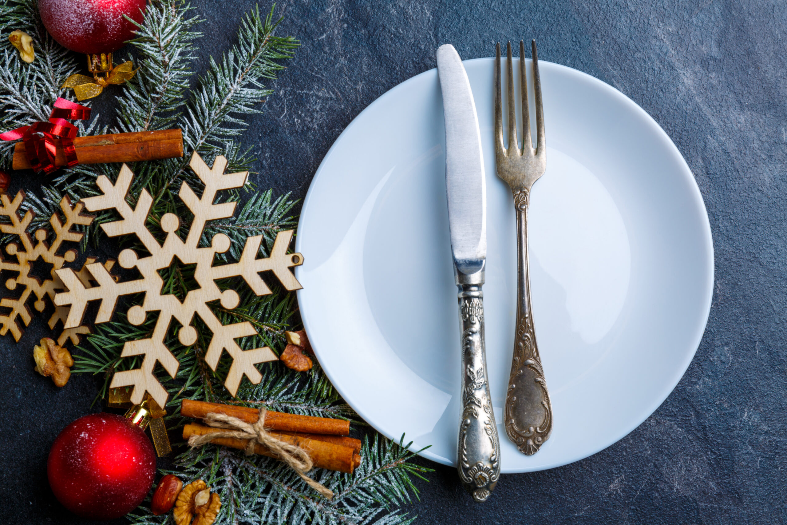 White round plate with a table knife and fork, next to a branch of a Christmas tree decorated with Christmas decorations.