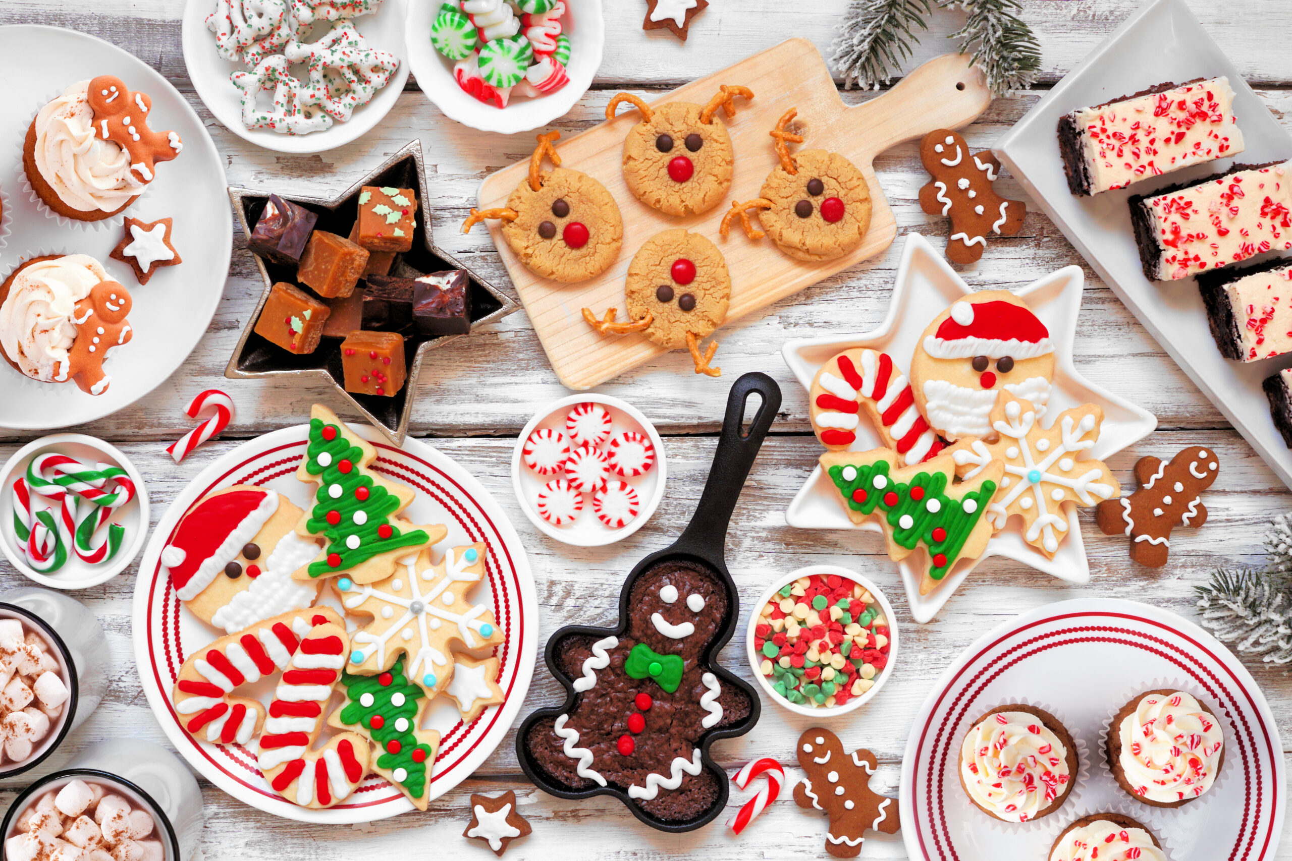 Cute Christmas sweets and cookie table scene. Top down view over a rustic white wood background. Fun holiday baking concept.